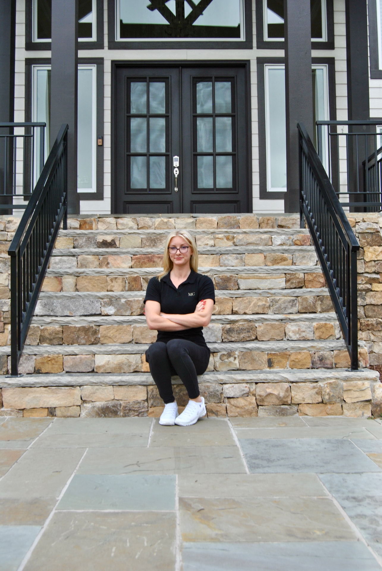 Madalyn, founder of Madalyn's Cleaning Co., sitting on stone steps in front of a luxury home
